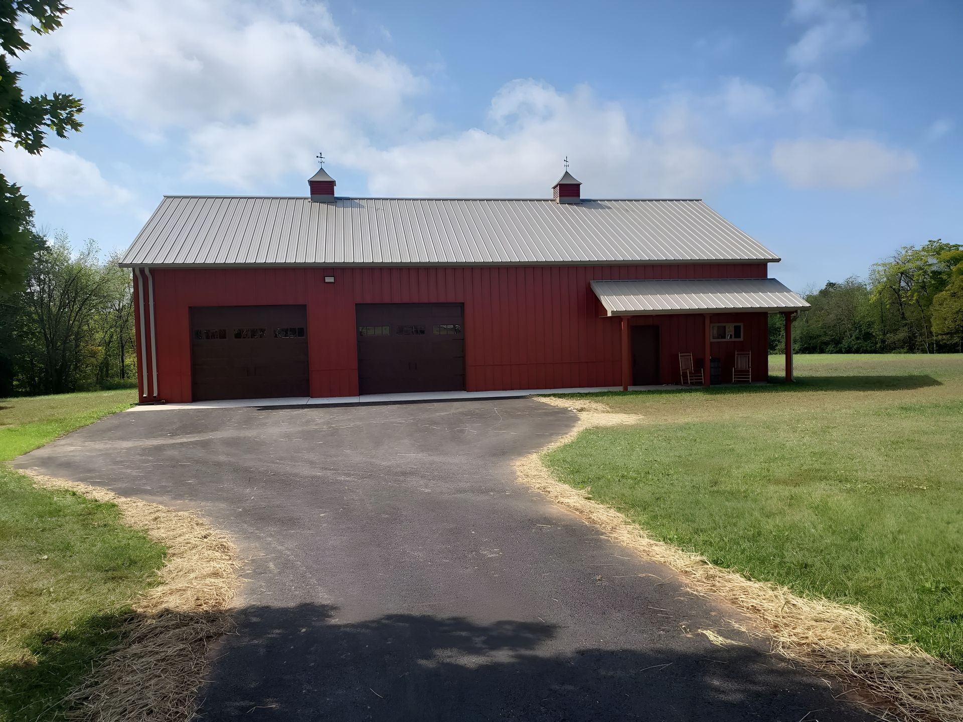 A red barn-style building with two garage doors and an attached side porch, situated on a grassy lot with a driveway.