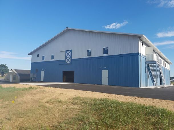 Large metal warehouse building with blue lower walls and white upper walls, featuring a side entrance and exterior stairs.