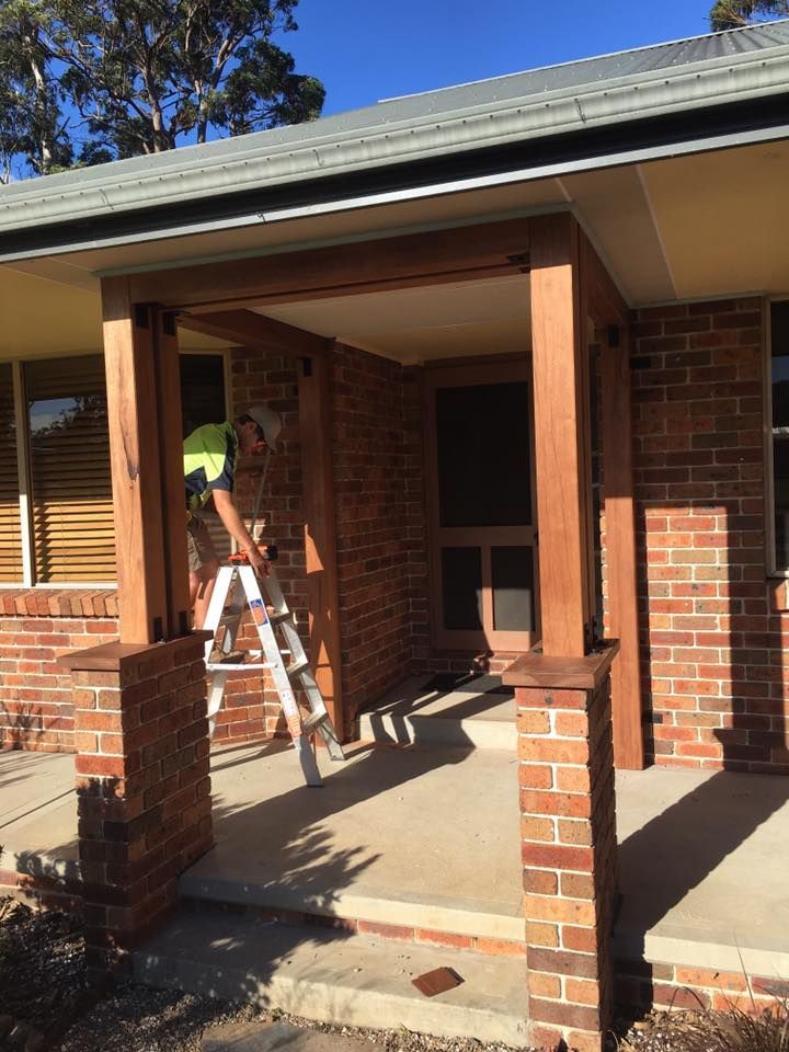 A Man is Standing on a Ladder in Front of a Brick House — LVL Constructions in Newcastle, NSW