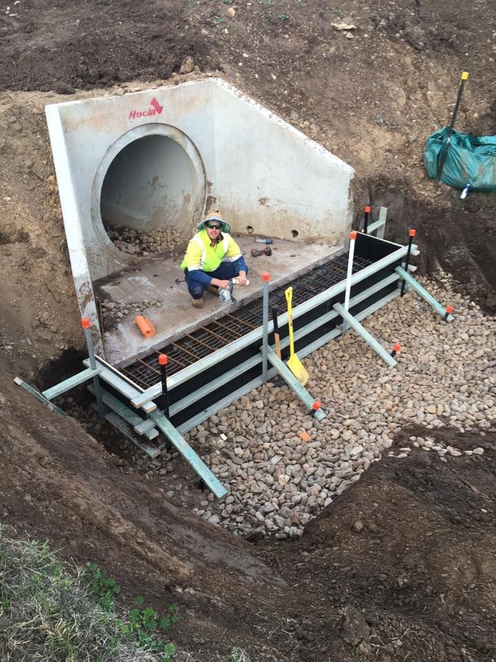 A Man is Kneeling in the Dirt Next to a Large Pipe — LVL Constructions in Newcastle, NSW