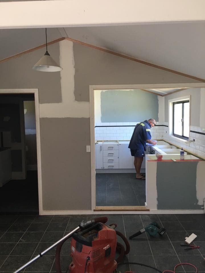 A Man is Working in a Kitchen With a Vacuum Cleaner in the Foreground — LVL Constructions in Newcastle, NSW
