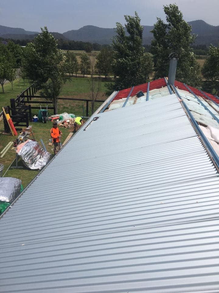 A Metal Roof is Being Installed on a House With Mountains in the Background — LVL Constructions in Newcastle, NSW