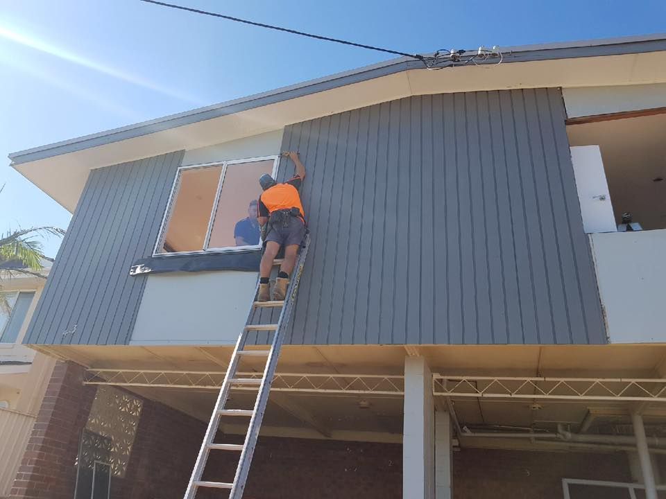A Man is Standing on a Ladder on the Side of a House — LVL Constructions in Newcastle, NSW