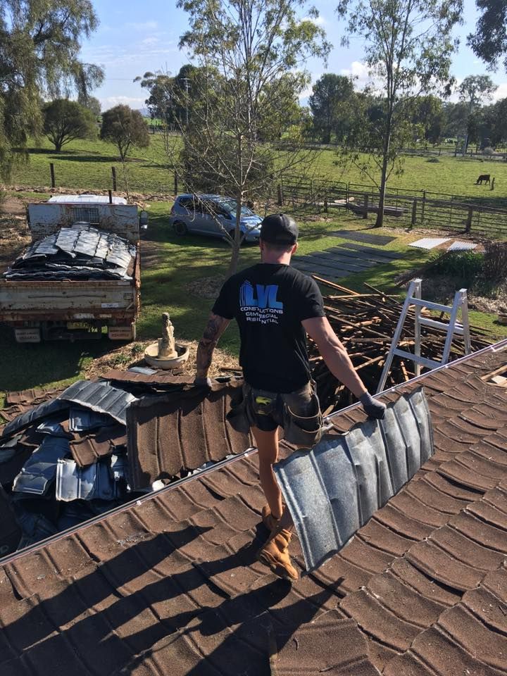A Man is Standing on Top of a Roof Holding a Piece of Metal — LVL Constructions in Newcastle, NSW