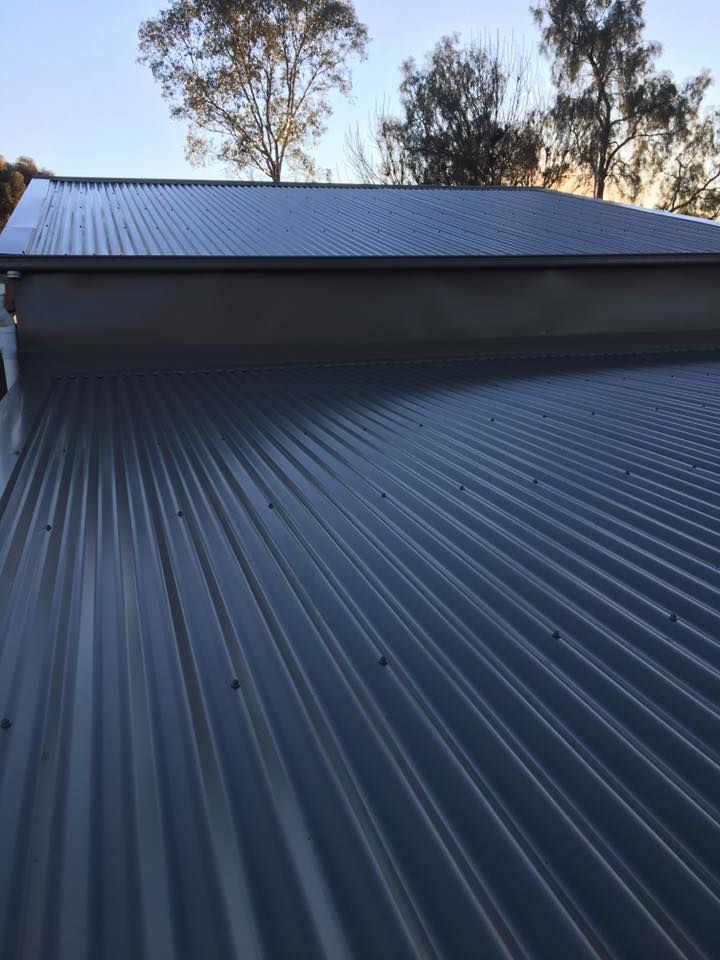 A Close Up of a Black Corrugated Metal Roof With Trees in the Background — LVL Constructions in Newcastle, NSW