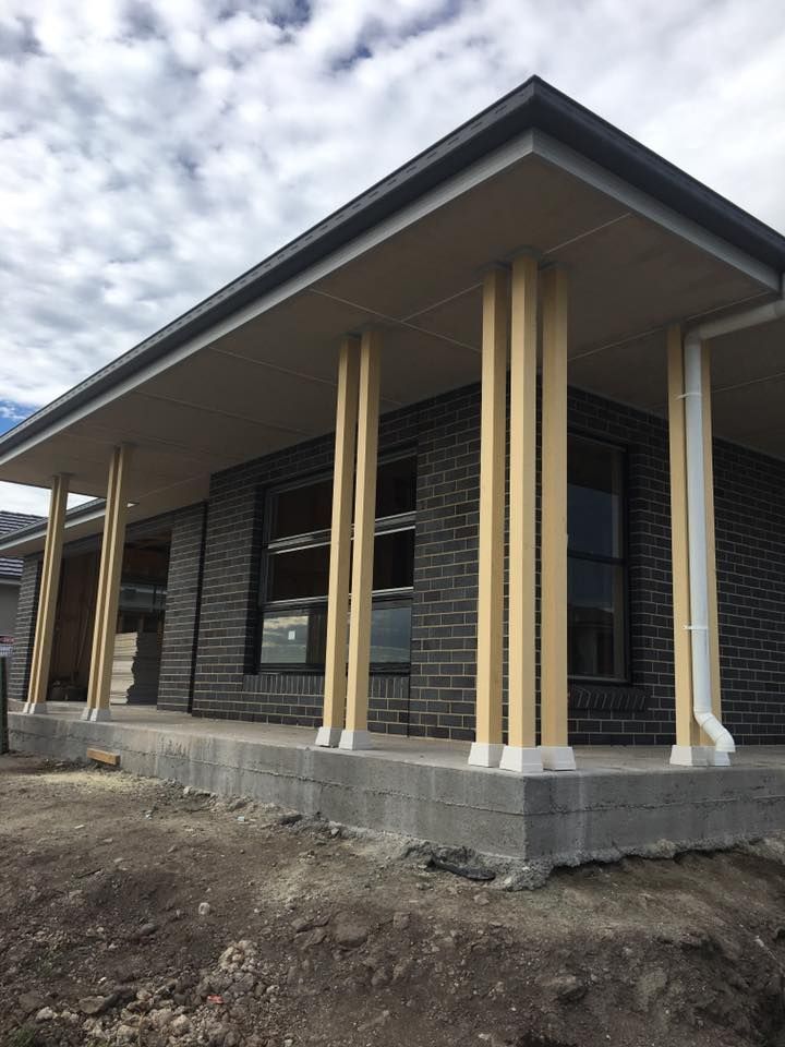 A Brick House With a Porch and Wooden Pillars — LVL Constructions in Newcastle, NSW