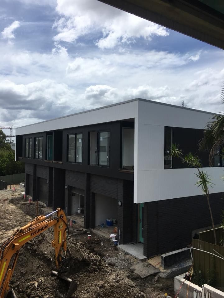 A Large Building is Being Built With a Yellow Excavator in Front of It — LVL Constructions in Newcastle, NSW