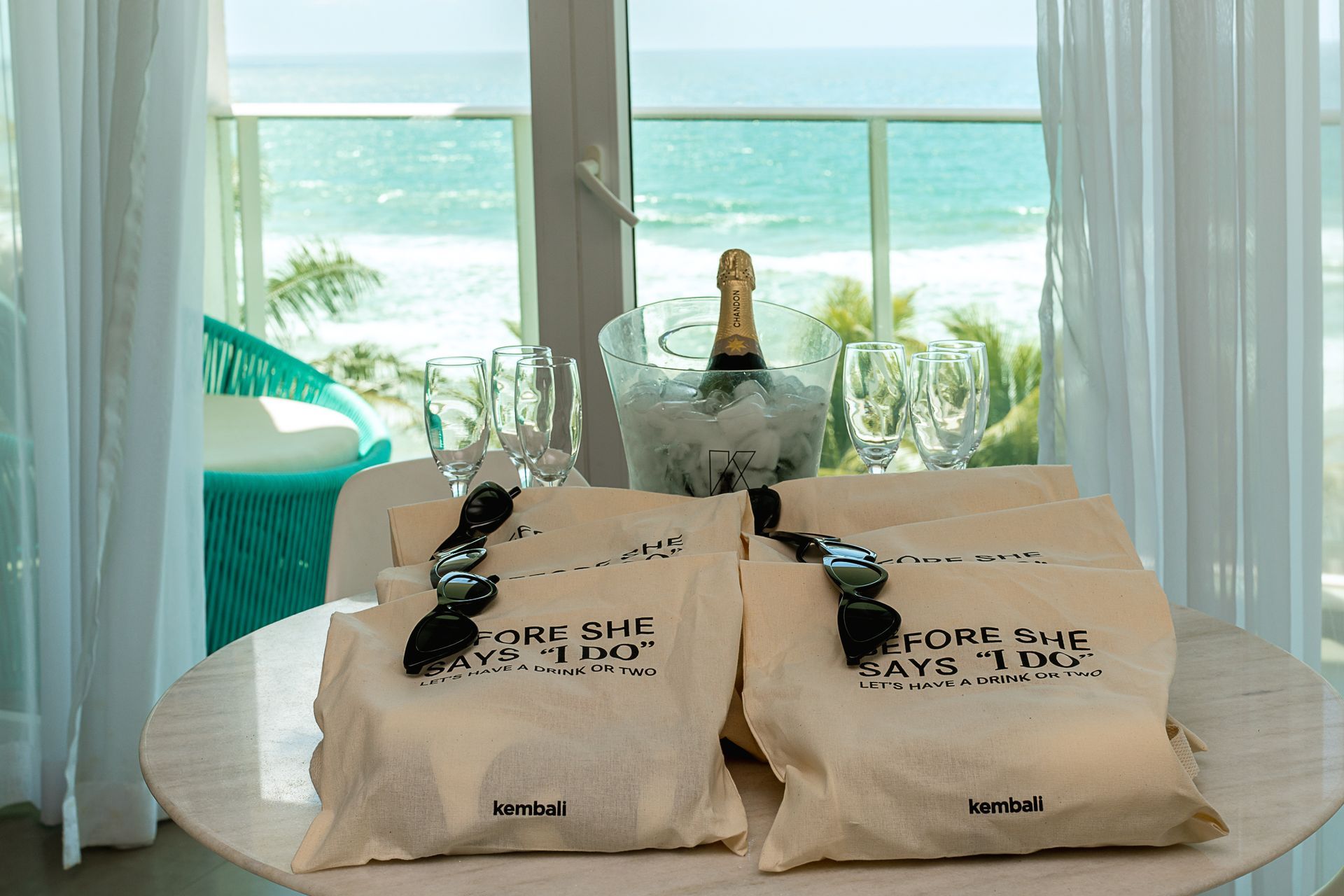 Kit de despedida de solteira do Kembali Hotel com taças, espumante e brindes personalizados em mesa com vista para o mar.