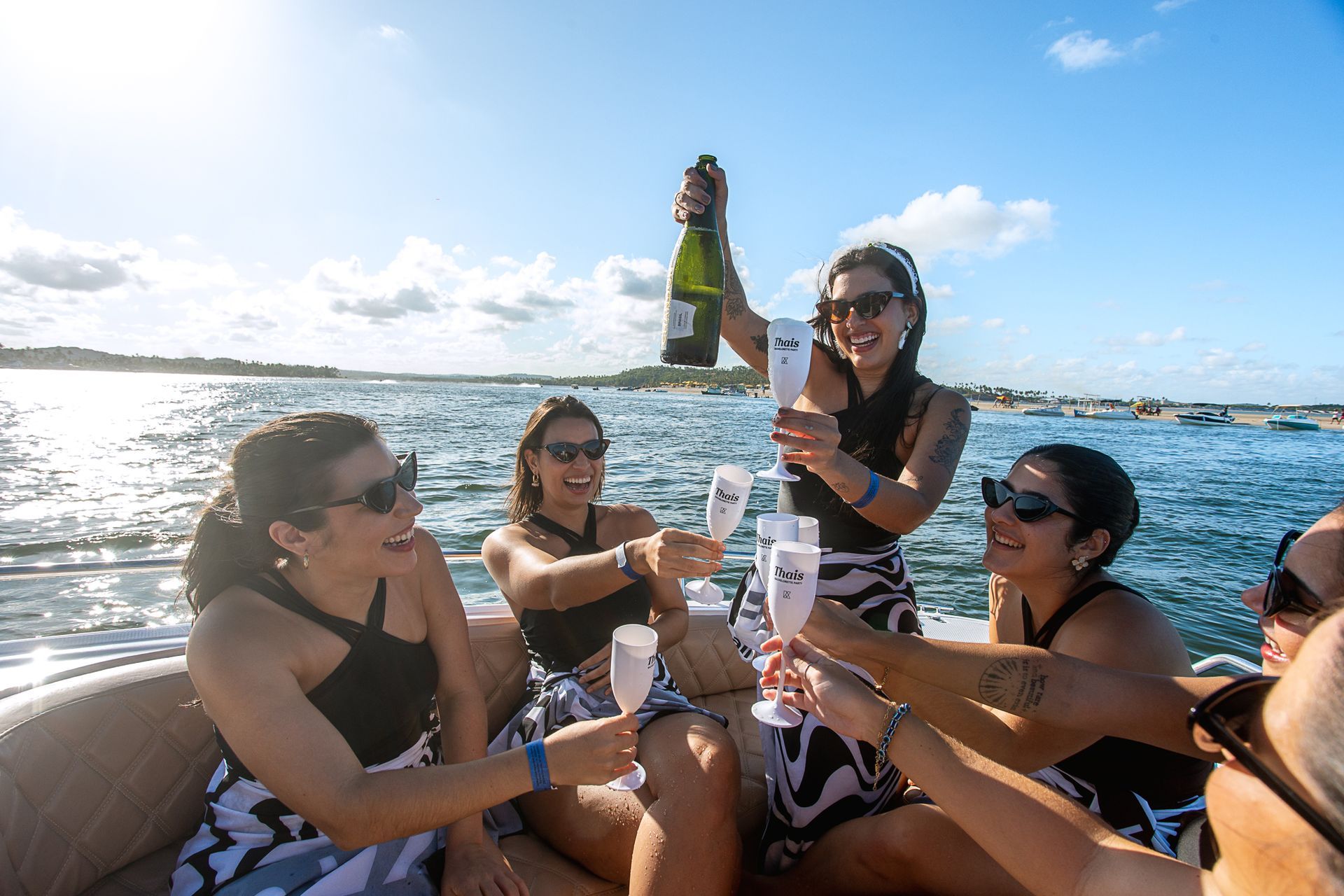 Noiva comemora sua despedida de solteira em passeio de lancha em Porto de Galinhas, brindando com espumante ao lado das madrinhas no mar.
