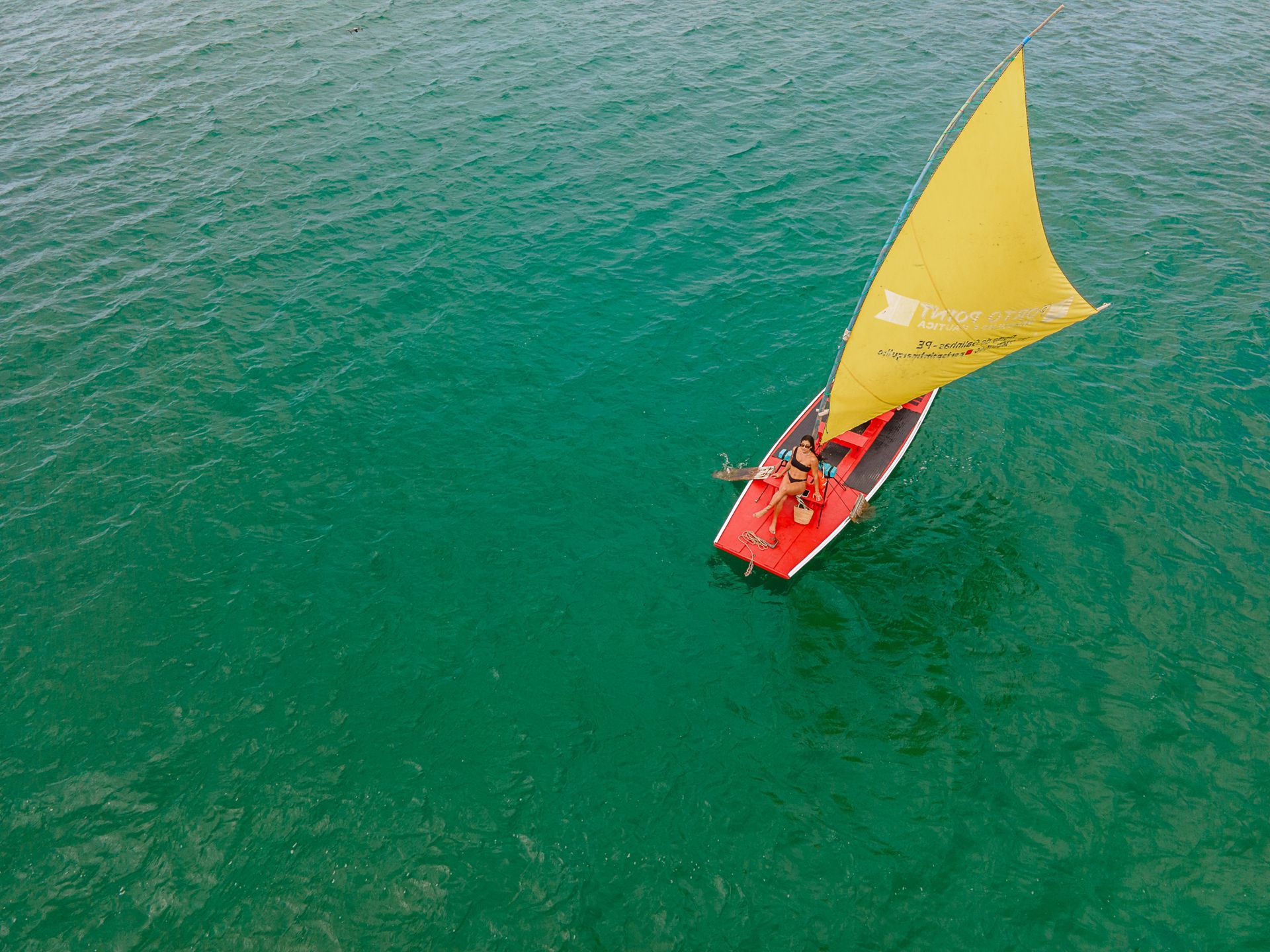 Visão aérea do mar de Porto de Galinhas, com uma jangada vermelha com vela amarela.