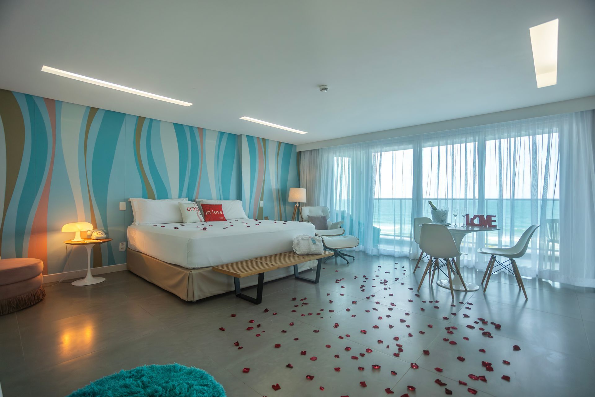 Quarto romântico com cama decorada com pétalas, vista para o mar, mesa posta e iluminação suave em a