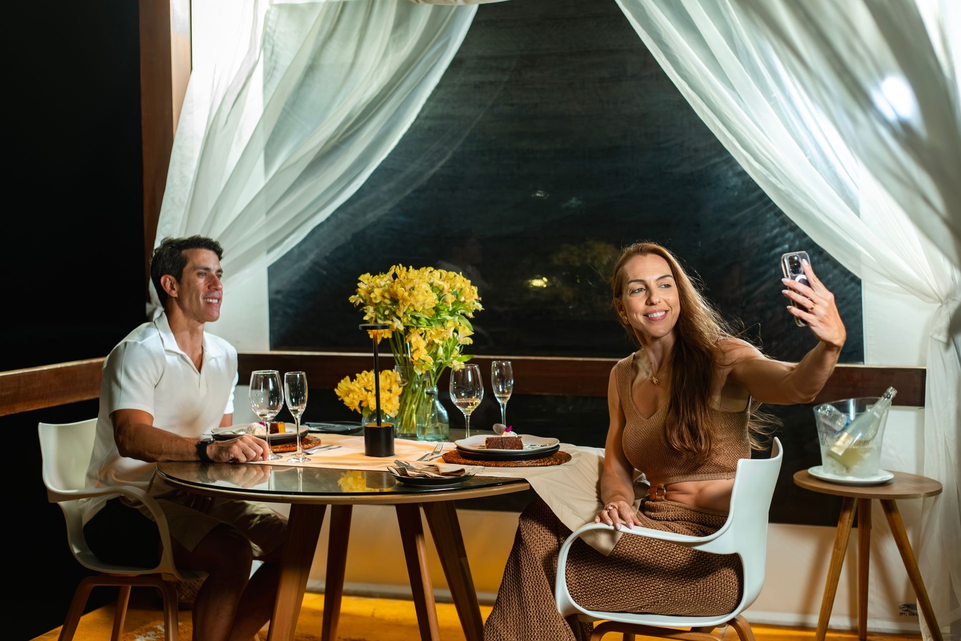 área externa de hotel à noite com iluminação decorativa, gazebo, coqueiros, almofadas no gramado e cadeiras