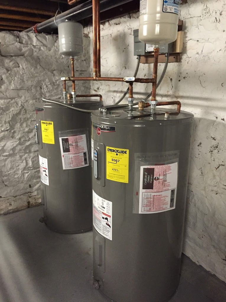 Two water heaters are sitting next to each other in a basement.