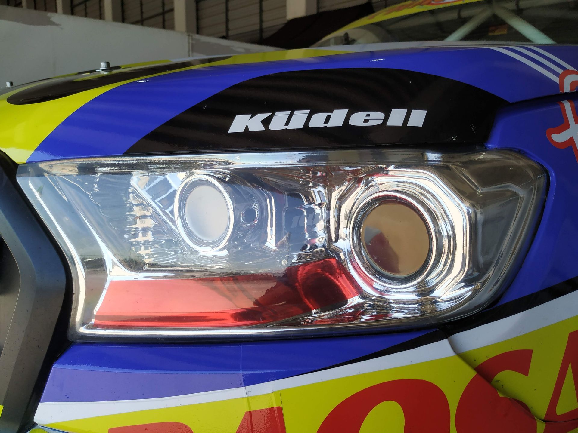 Primer plano de un faro de coche con gráficos azules, amarillos y negros. Encima del faro está escrito 