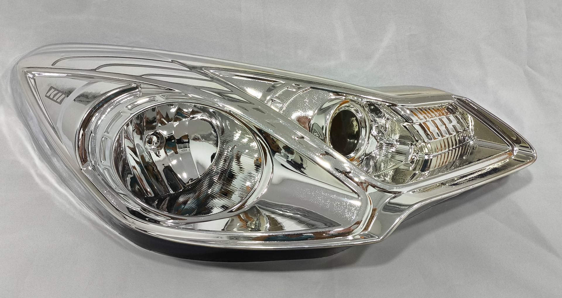 Faro cromado de coche sobre una superficie neutra.