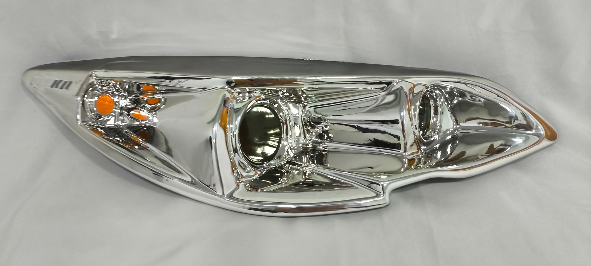 Faro cromado de coche sobre fondo blanco, inclinado hacia la derecha.
