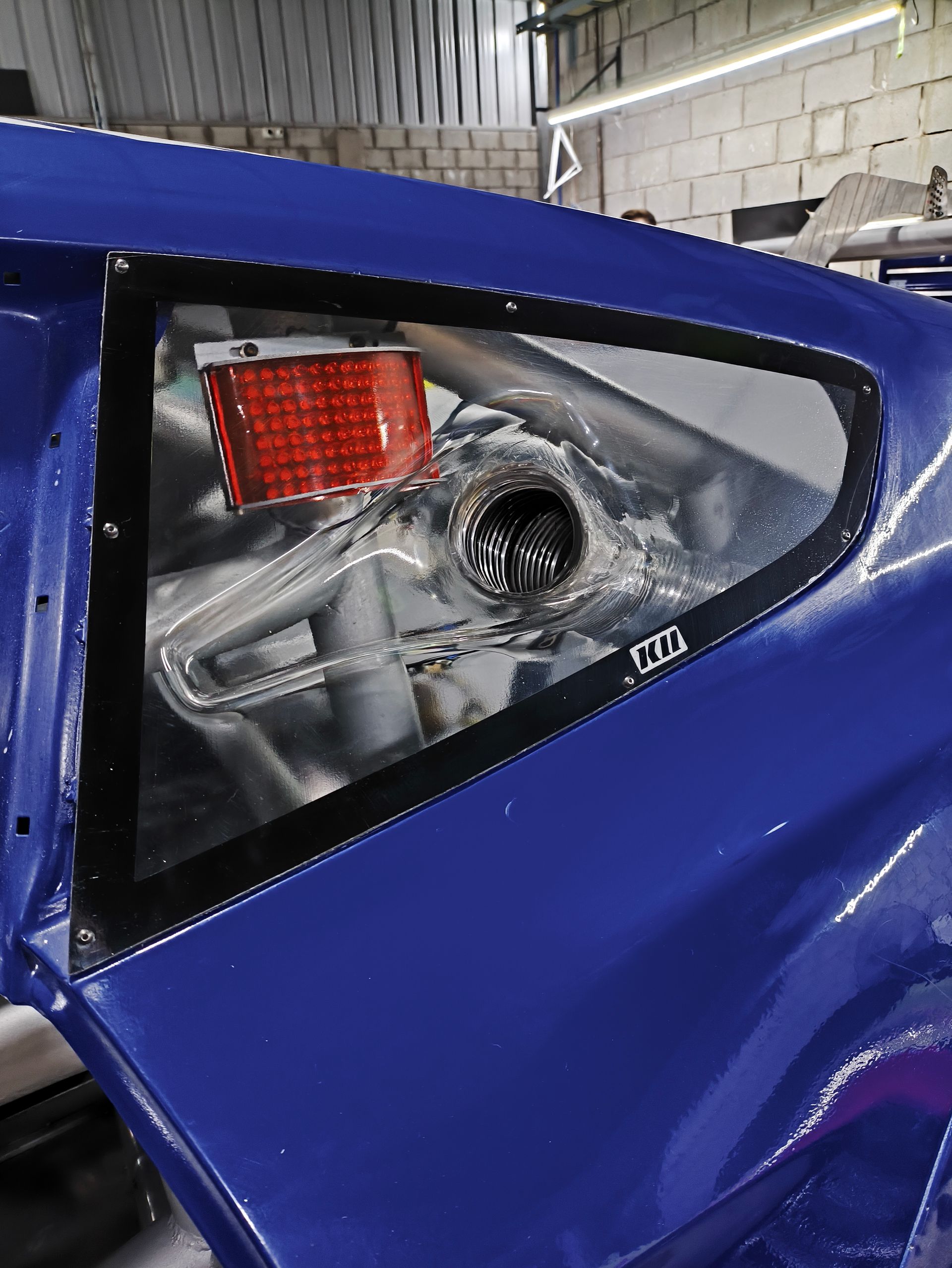 La ventanilla lateral del coche azul deja ver la jaula antivuelco y el depósito de combustible