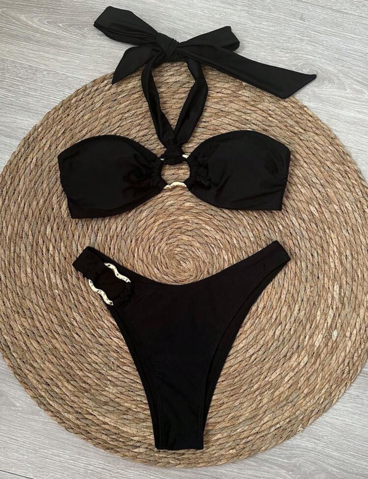 Mujer en bikini negro con detalles de anillos dorados.