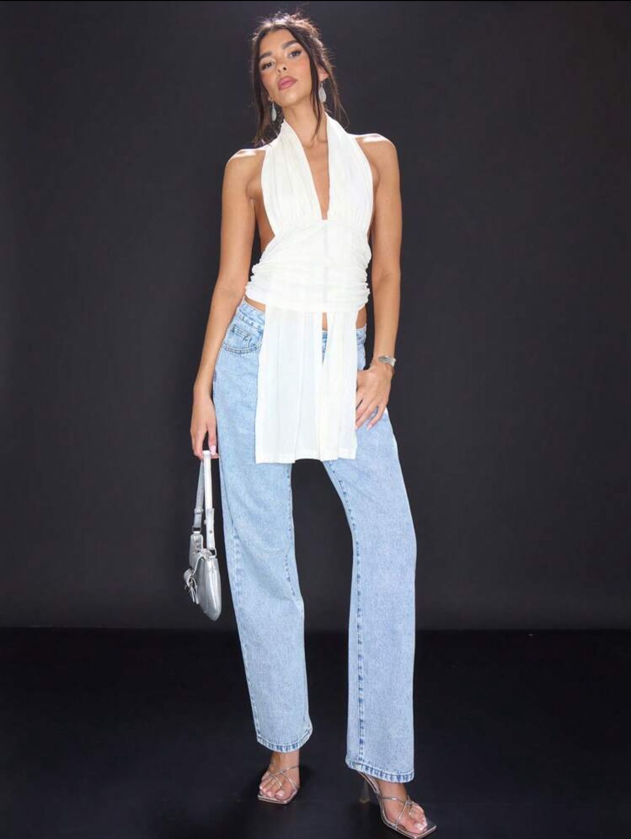 Mujer con top sin espalda y jeans sobre un fondo negro.