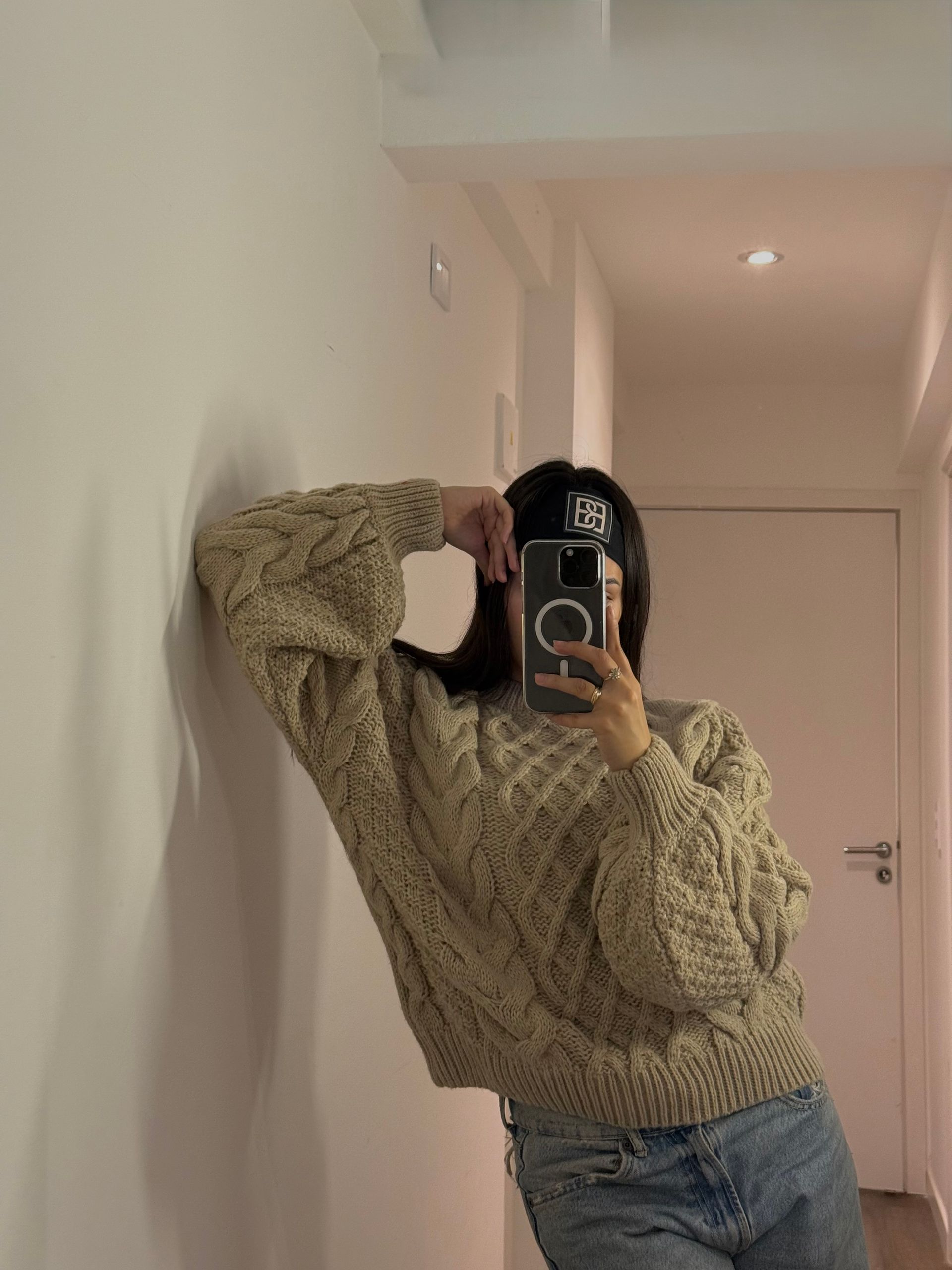 Persona que viste un suéter de punto cable color crema con una extensión de falda gris, sobre jeans.