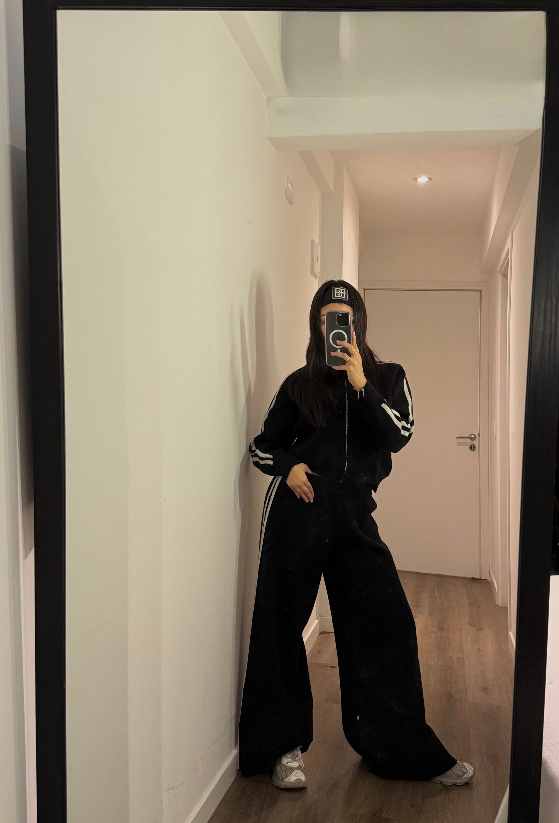 Persona con chándal Adidas tomándose un selfie frente al espejo en un pasillo.