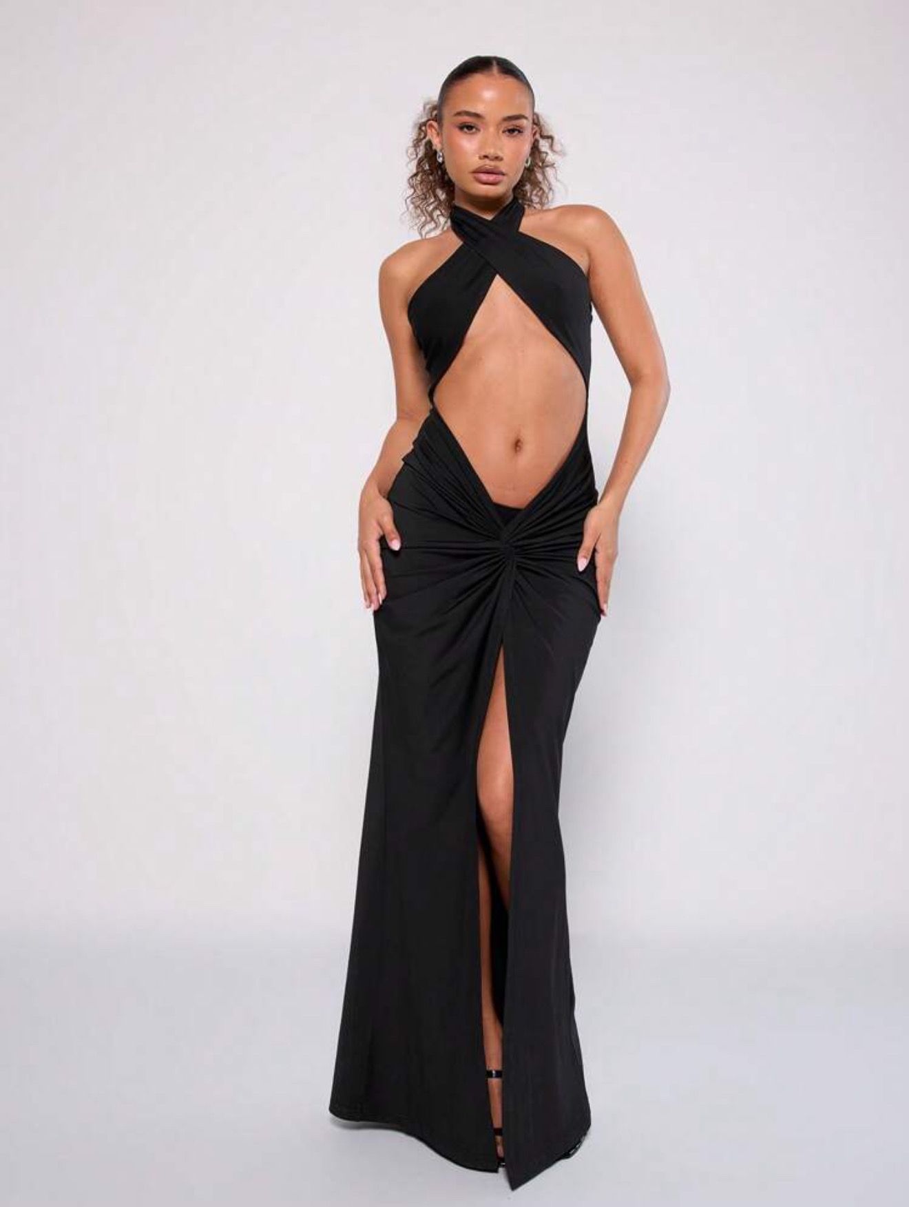 Mujer con un vestido negro con cuello halter, corpiño recortado y abertura alta, posando con las manos en las caderas.