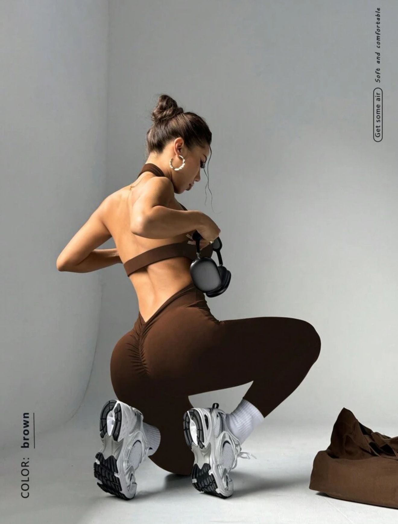 Una mujer con un vestido marrón y auriculares se encuentra frente a una pared con imágenes impresas.