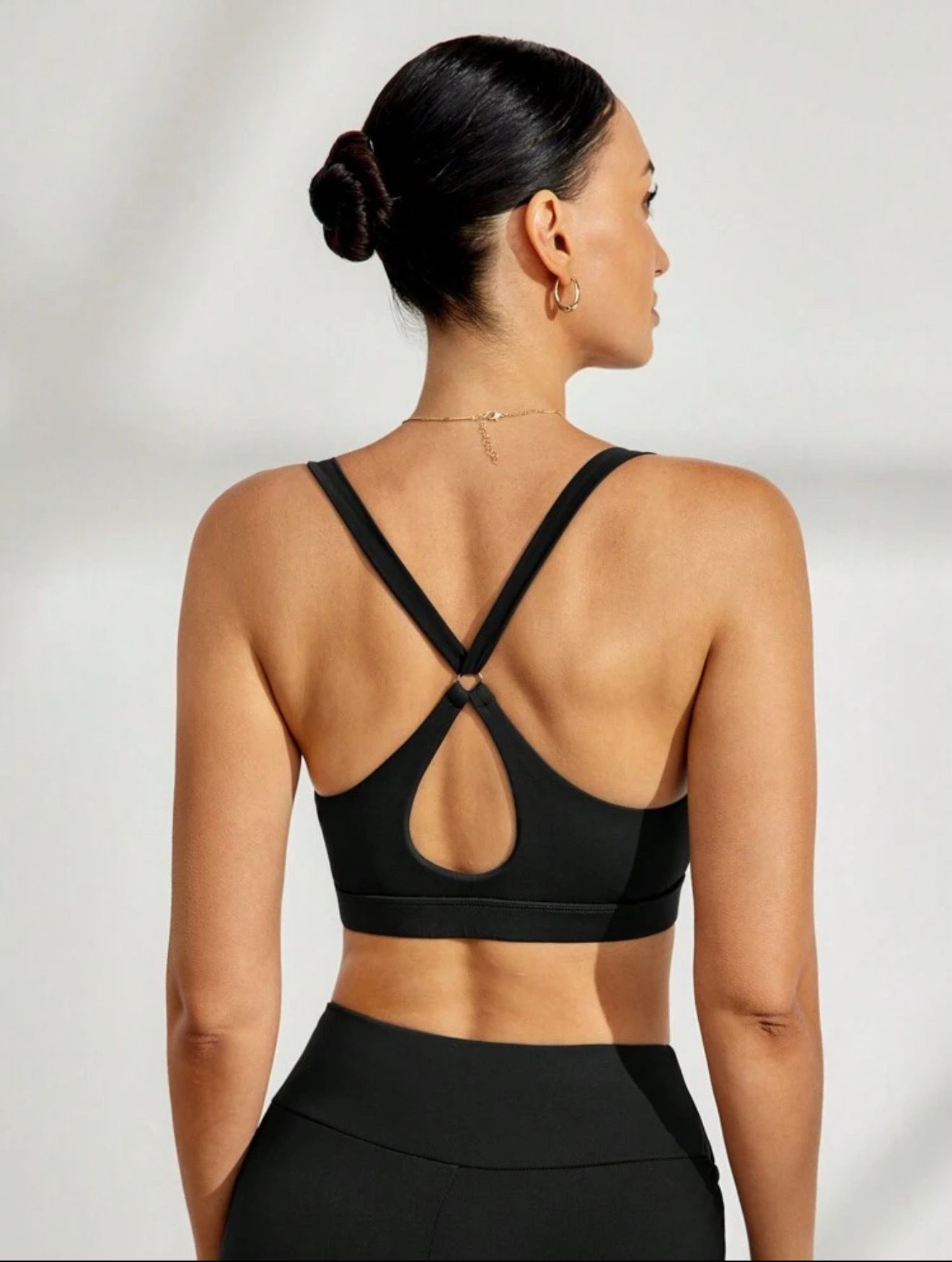 Mujer con sujetador deportivo negro con recorte, con collar, mirando fuera de cámara.