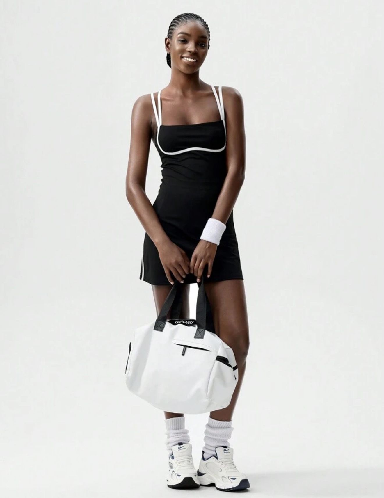 Mujer sonriendo, vistiendo un vestido deportivo negro con ribetes blancos, sosteniendo un bolso sobre su hombro.
