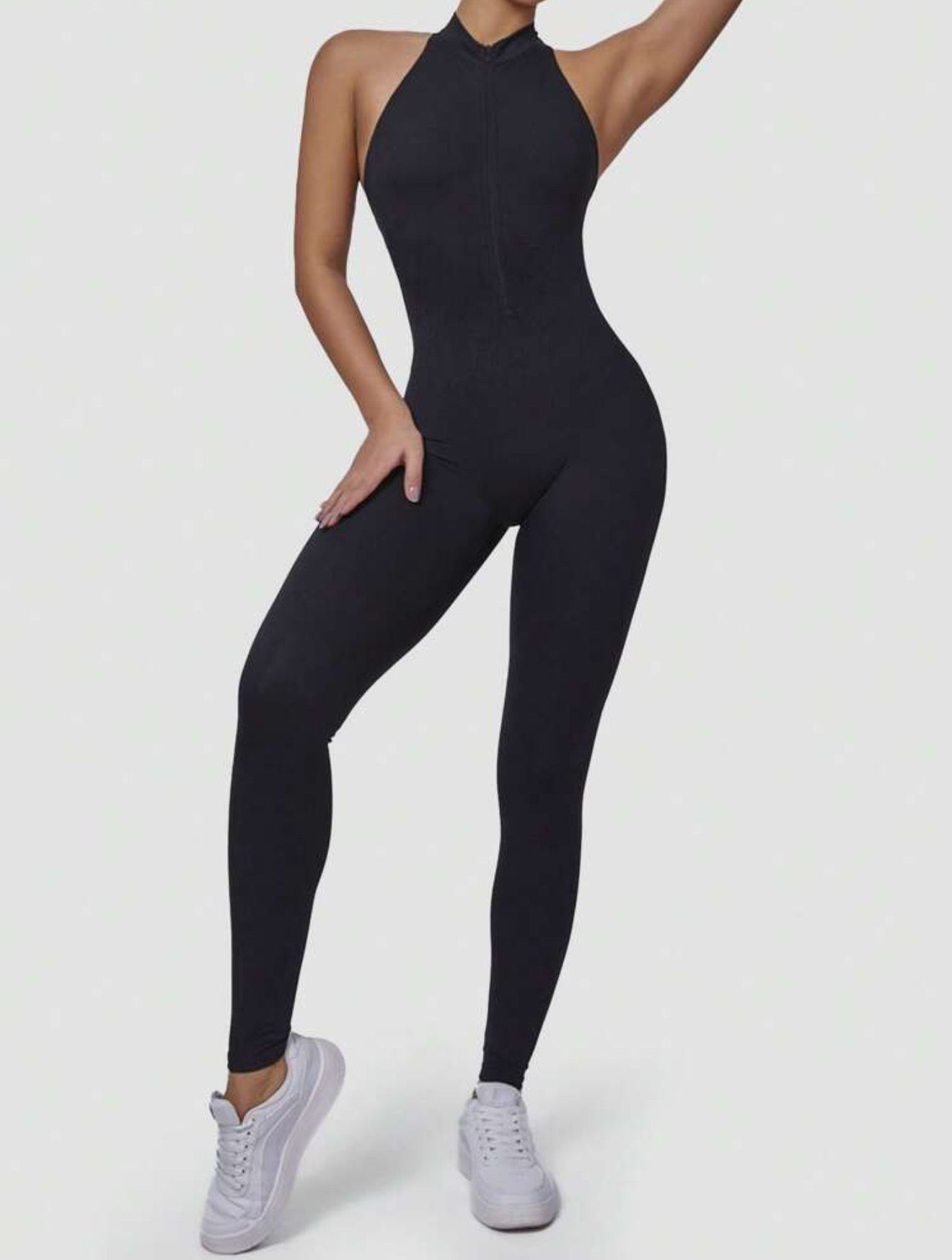 Mujer con mono deportivo negro sin espalda y zapatillas blancas.