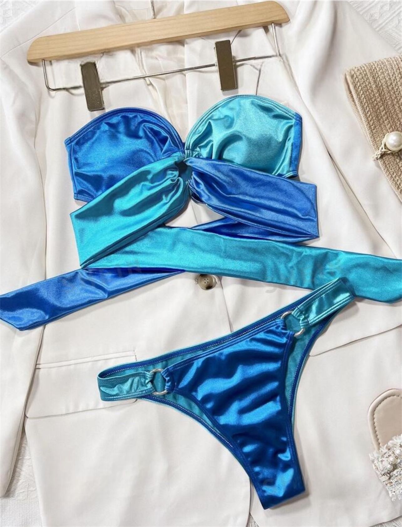 Mujer vistiendo un bikini verde azulado de dos tonos con detalles de anillos de metal, acostada sobre una superficie blanca.