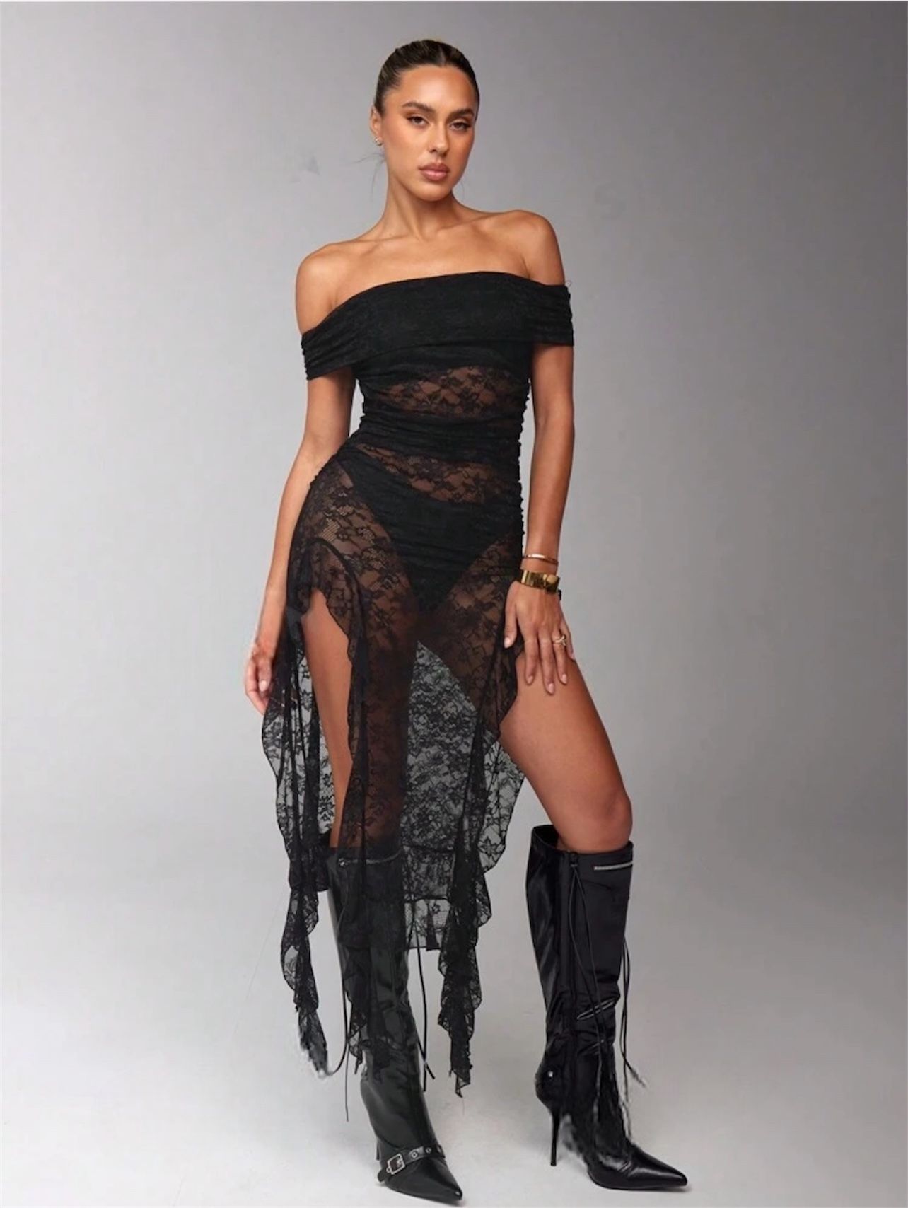 Mujer con vestido negro de encaje con hombros descubiertos. Abertura alta. Un brazo flexionado. Fondo claro.