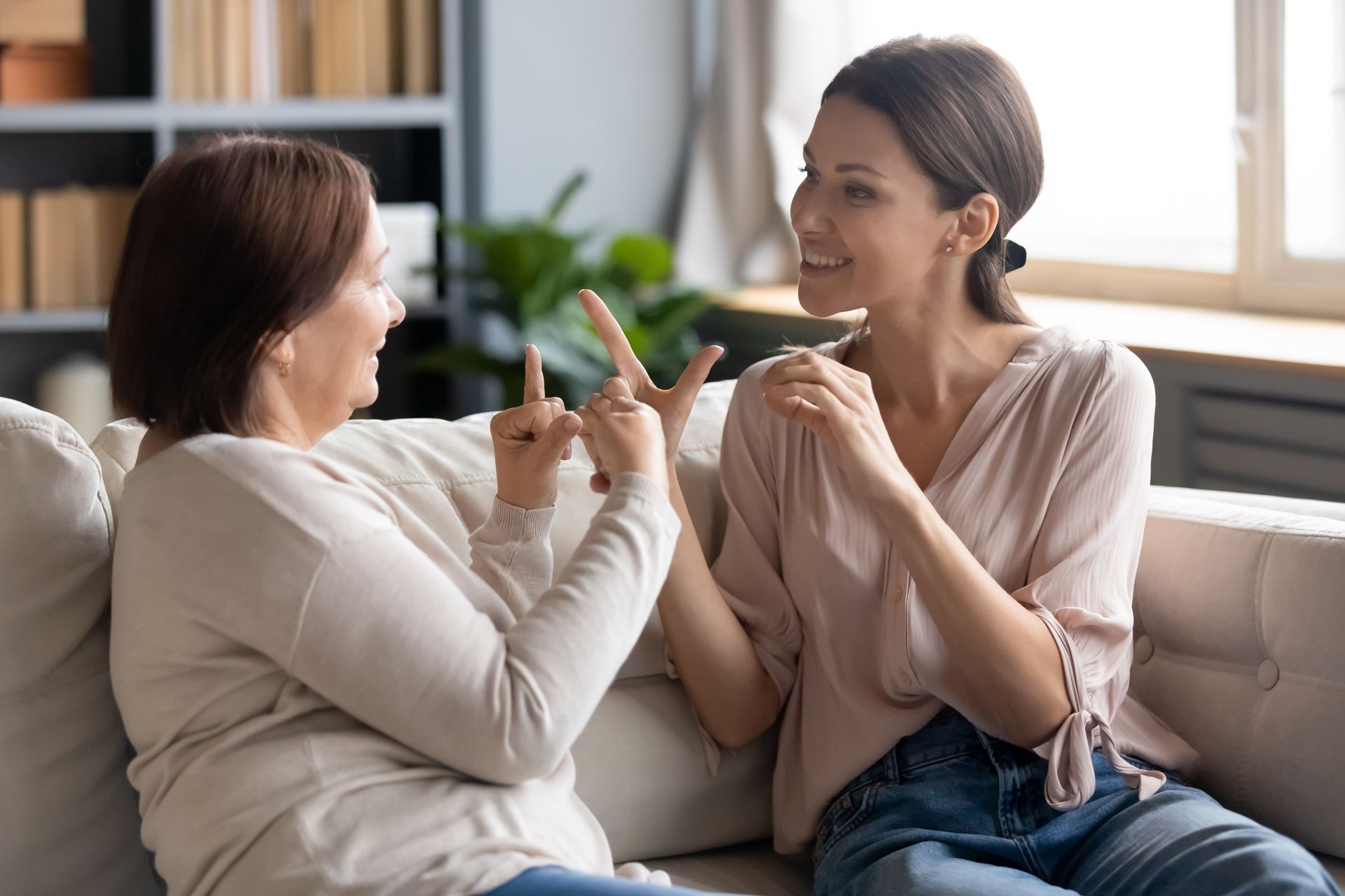 Two people signing on a couch, indoors. One points with index finger, the other smiles.