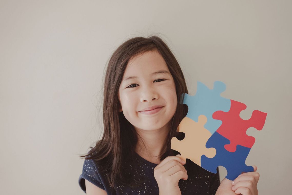 Girl smiling, holding colorful puzzle pieces.