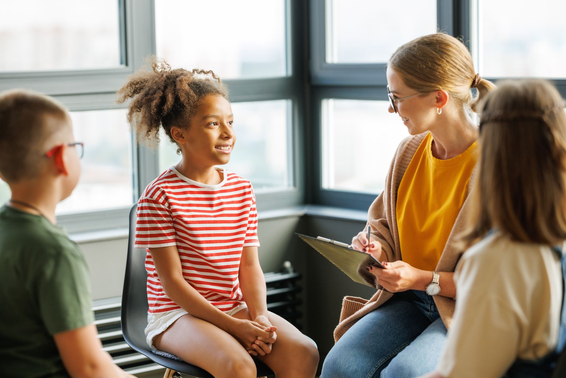 Children in a group therapy session with a counselor, sitting in chairs and talking.