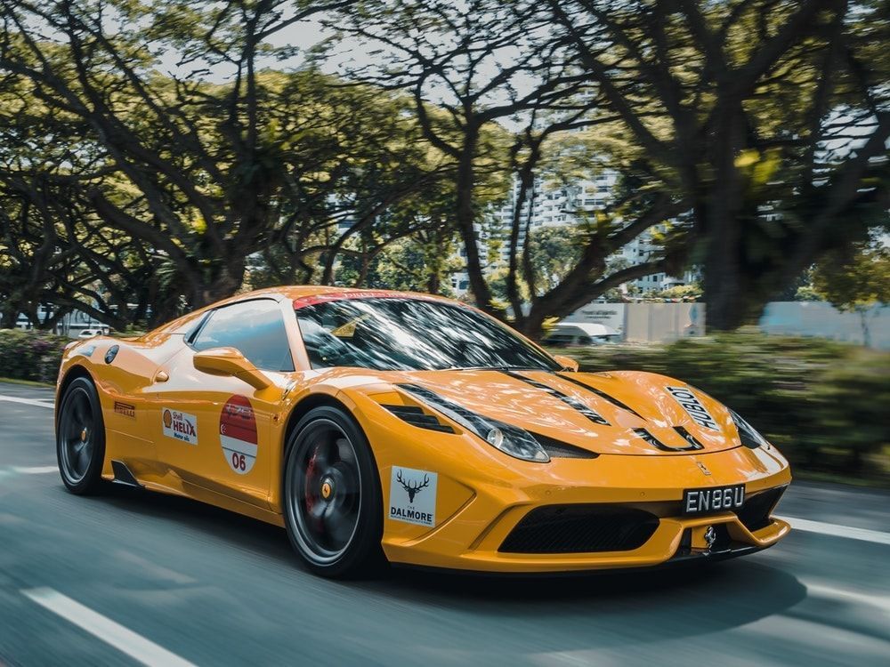 Yellow Ferrari sports car driving on a tree-lined road.