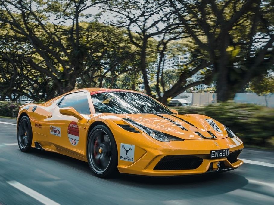 Yellow Ferrari sports car driving on a tree-lined road.