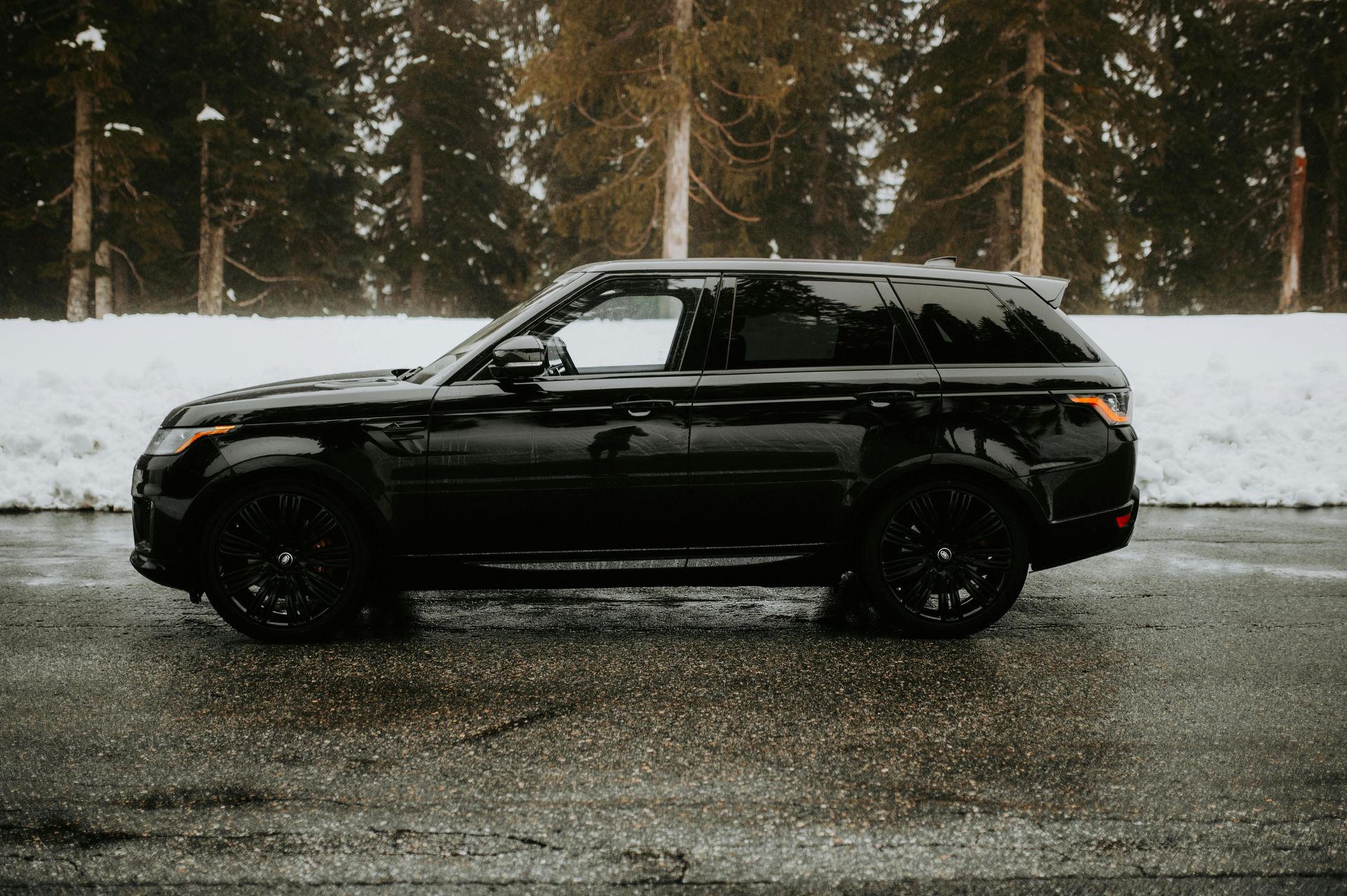Black Range Rover SUV parked on a wet road with snowy trees in the background.