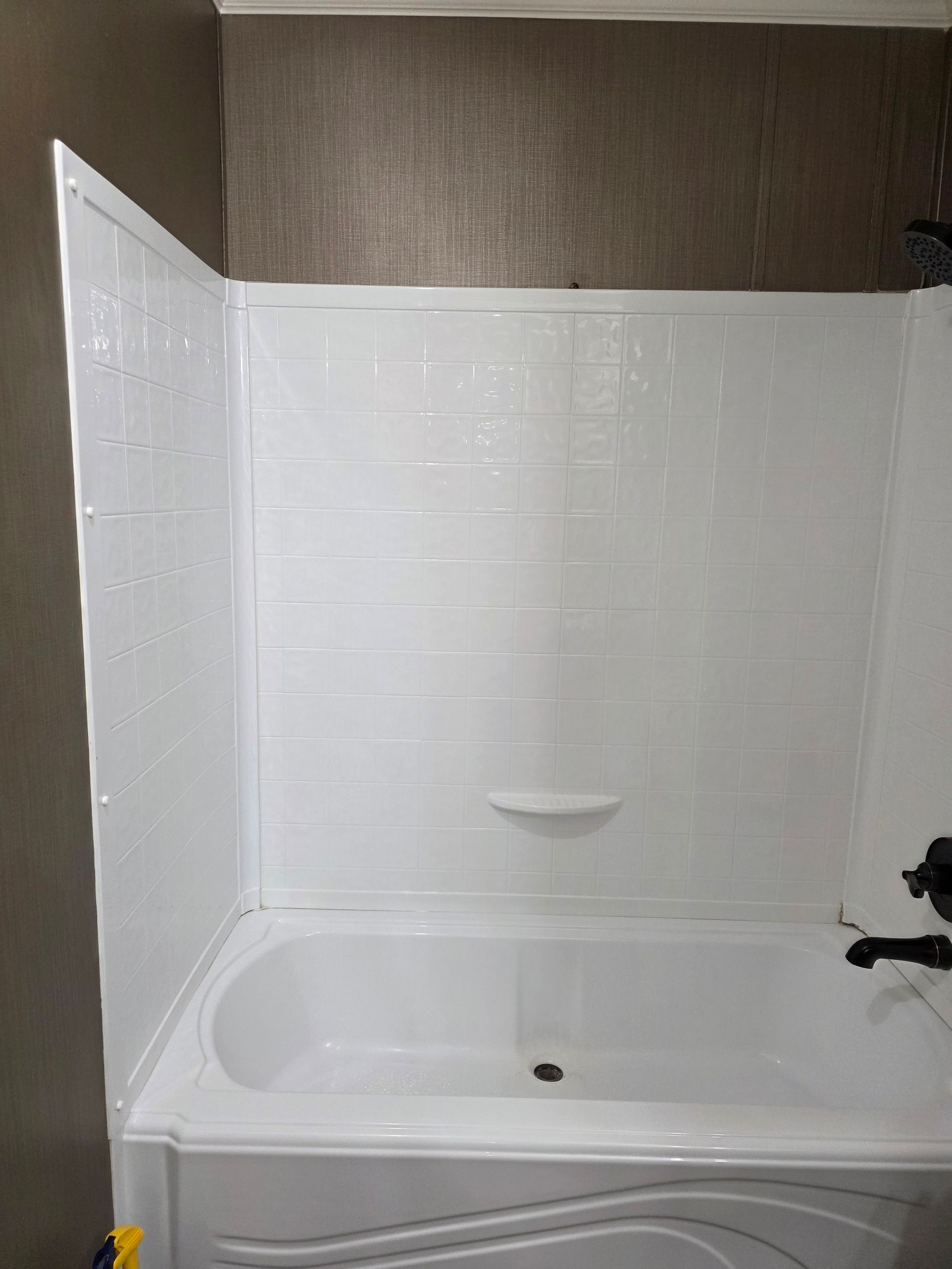 White bathtub and surround in a bathroom, with brown walls and a small built-in soap dish.