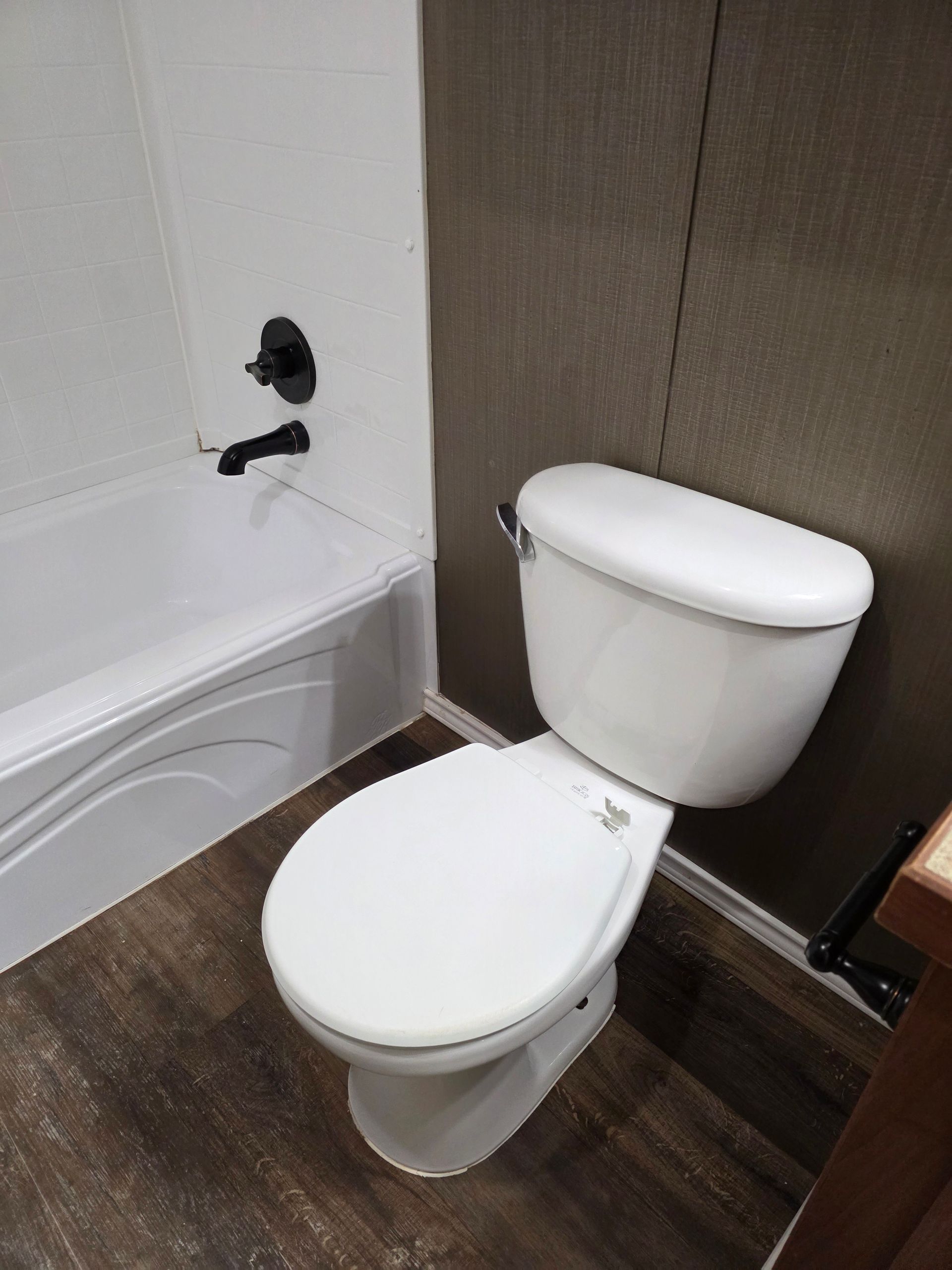 White toilet and bathtub in a bathroom with dark-colored wood-like flooring and dark fixtures.