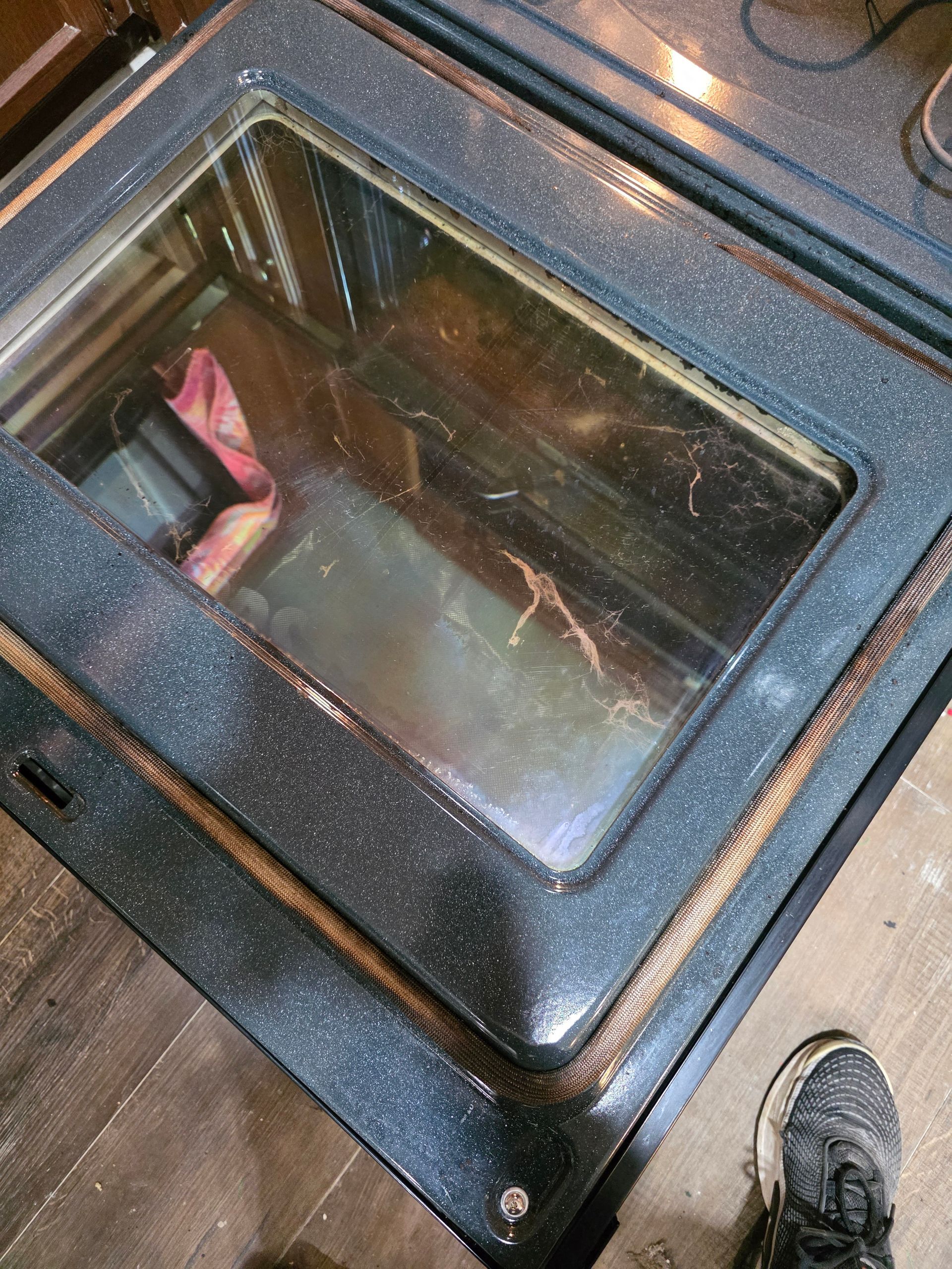 Close-up of oven interior with dirty glass and surrounding speckled black surface.