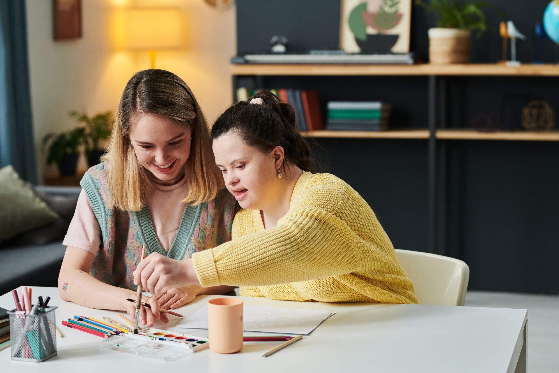 A woman is teaching a girl with down syndrome how to draw.