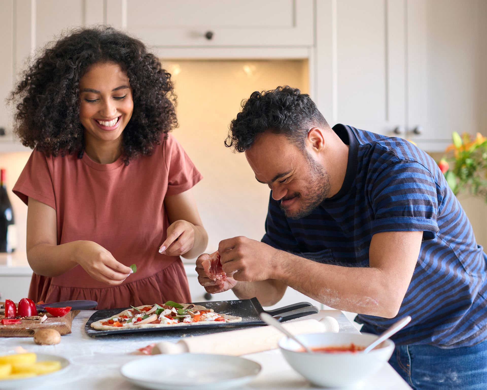 A man and a woman are making a pizza together in a kitchen.