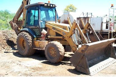 A yellow case backhoe is parked in a dirt field