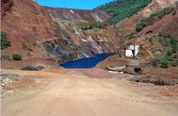 A dirt road leads to a large body of water surrounded by mountains