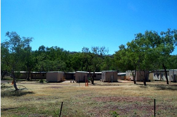 A row of houses in a field with trees in the background