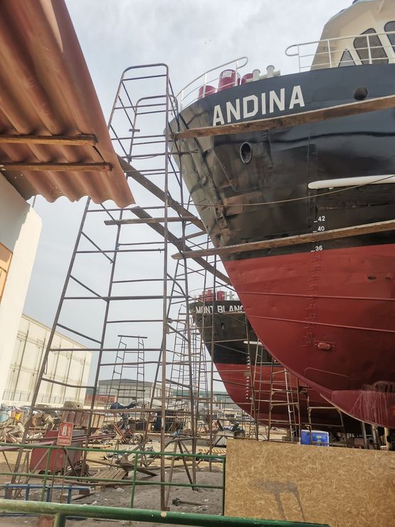 Astillero con grandes barcos en construcción, incluyendo una proa negra con la etiqueta 