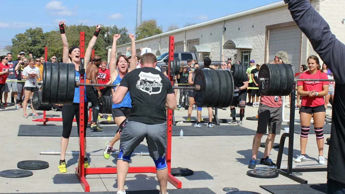People celebrating a successful barbell squat lift at an outdoor weightlifting competition.