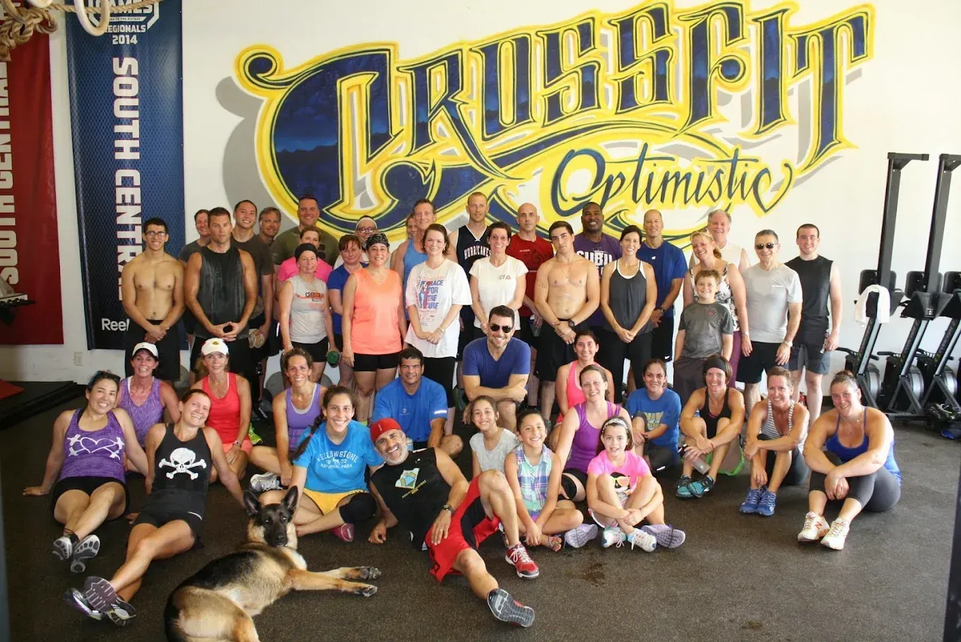 Group of people in a CrossFit gym, posing with a dog. CrossFit logo on the wall.