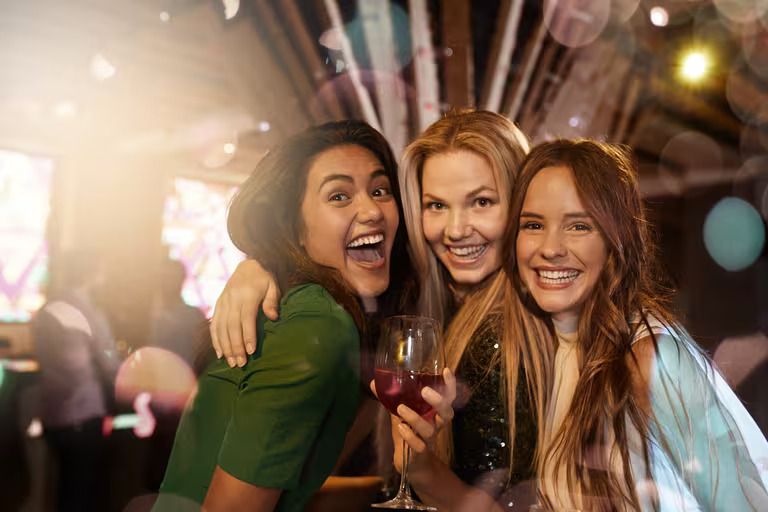 Three women are standing next to each other in a bar holding wine glasses.